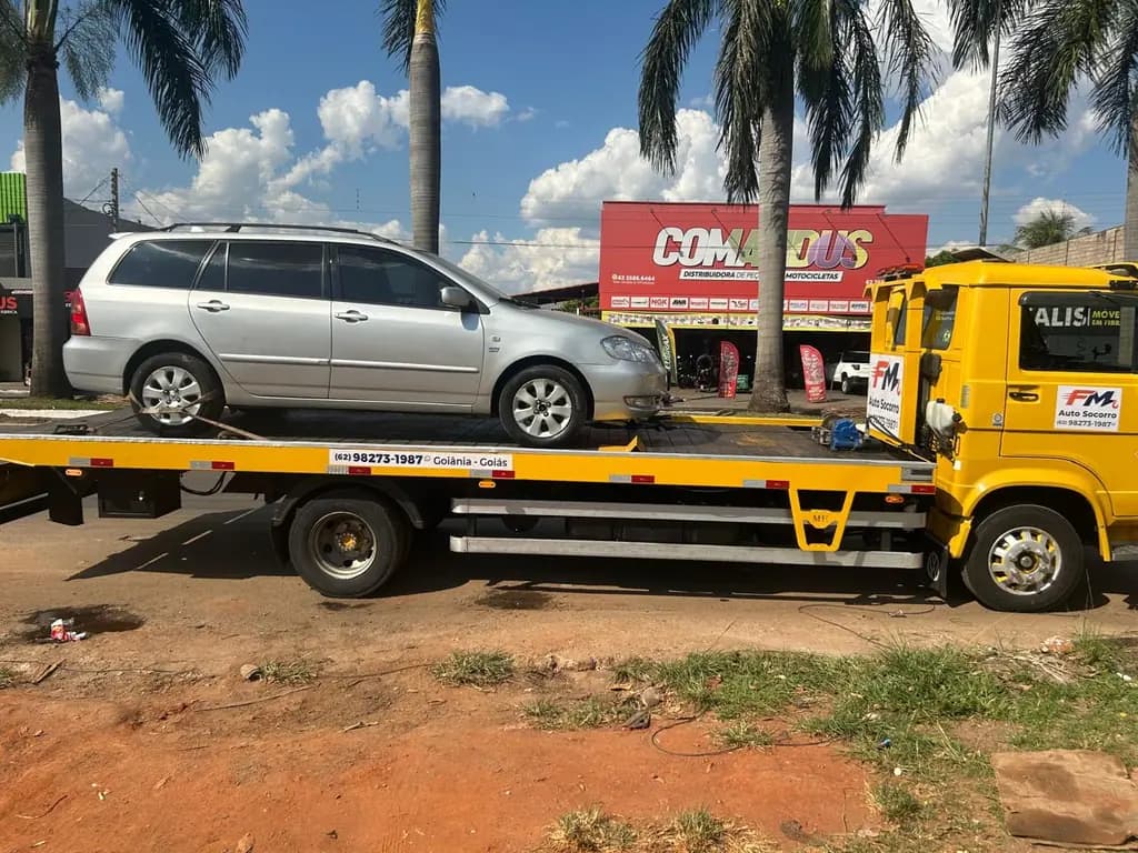 Perua Toyota Corolla Fielder prata sobre o guincho plataforma amarelo da FM Auto Socorro, à beira de uma avenida com palmeiras