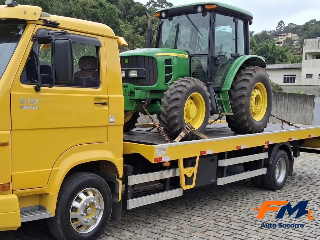 Trator agrícola verde e amarelo preso com correntes no guincho plataforma amarelo da FM Auto Socorro